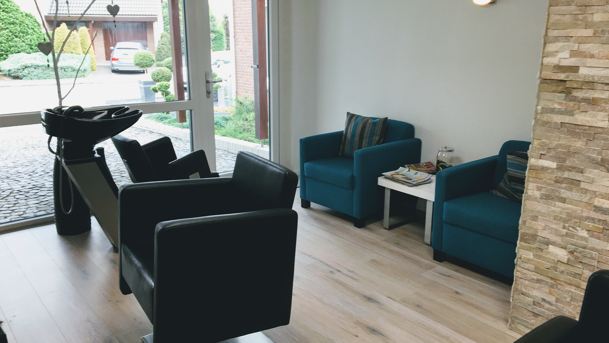 De salon: wasplek met zwarte stoelen, twee groene fauteuils en een natuurstenen wand