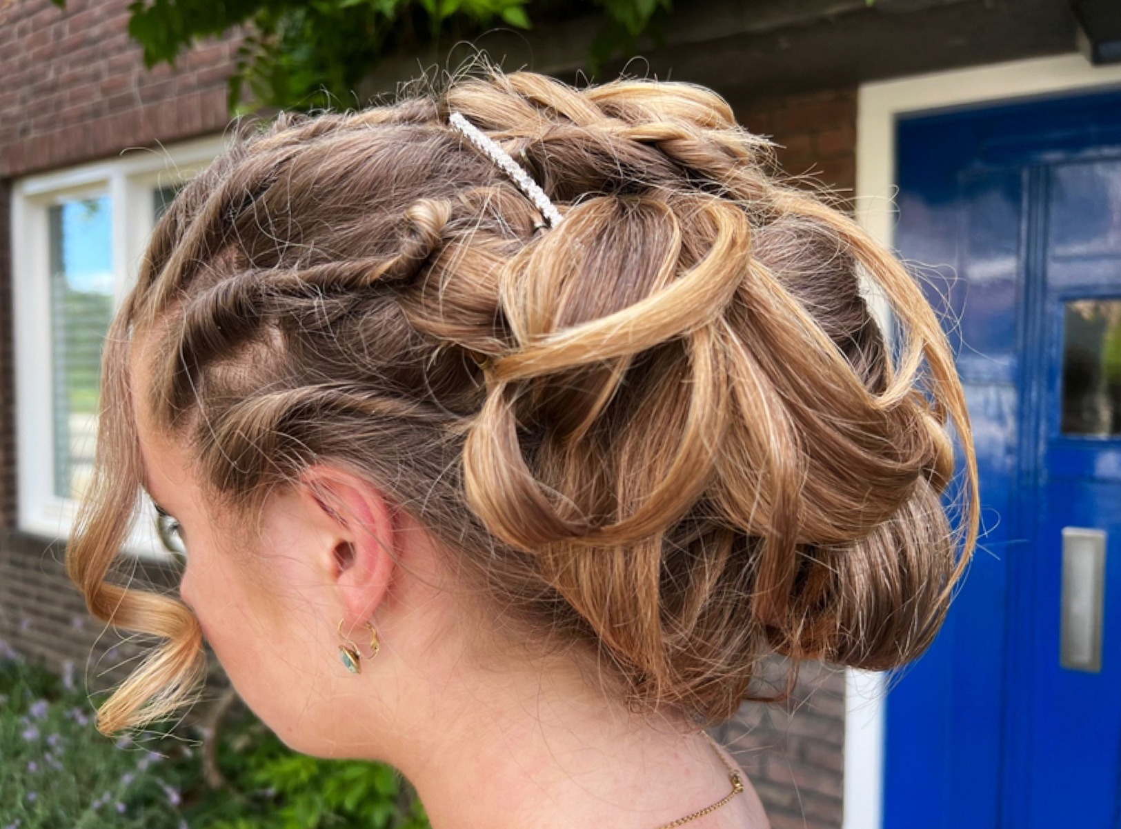Opgestoken kapsel met krullen en een parelspeld, voor een blauwe deur